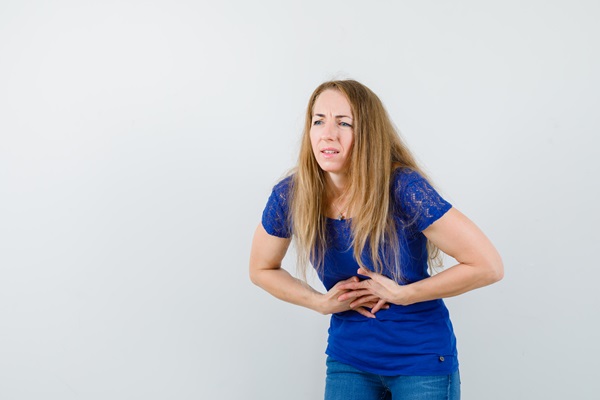 Mujer de cabello rubio sostiene su manos sobre el estómago haciendo una expresión de dolor