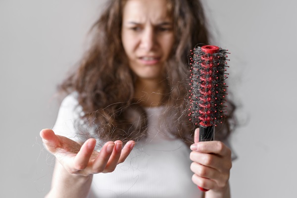 Mujer joven sostiene en sus manos un cepillo y cabello que se desprende durante el peinado