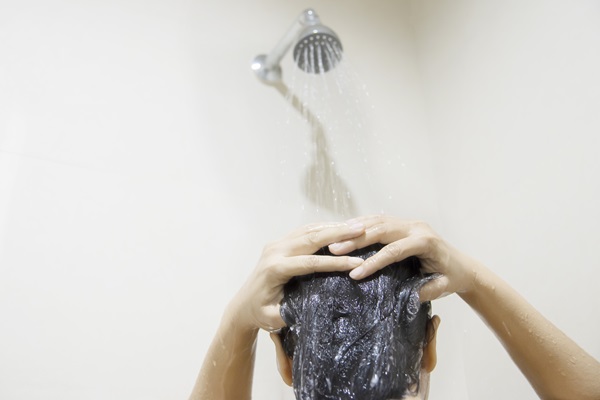 Mujer debajo de la ducha enjuaga su cabello con agua para retirar el champú
