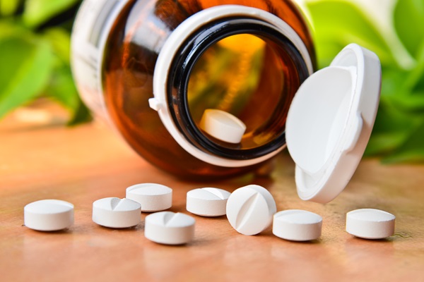 Espironolactona - Recipiente de vidrio con pastillas blancas circulares derramadas sobre una mesa de madera
