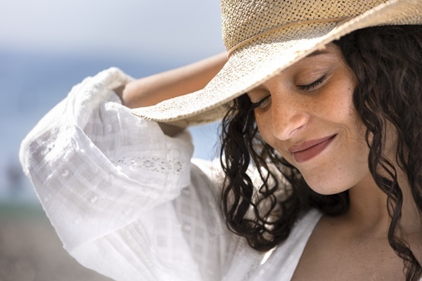 Caída del cabello - Mujer joven de cabello negro usa un sombrero para protegerse del sol