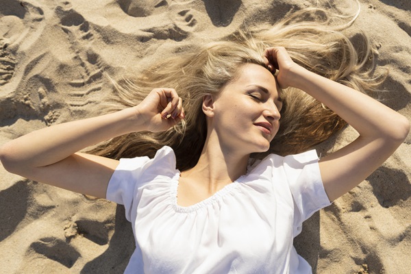 Caída del cabello - Mujer joven de cabello rubio acostada en la arena de la playa