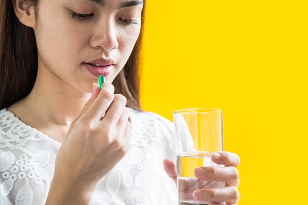 Mujer joven toma una pastilla y sostiene un vaso con agua en su mano