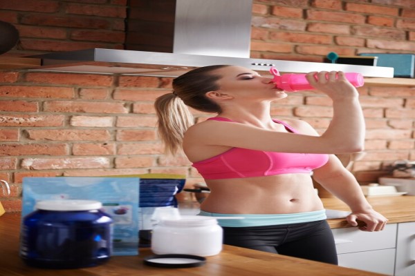 Batidos de proteína y calvicie - mujer en la cocina tomándose un batido de proteínas con productos para realizarlo sobre la encimera