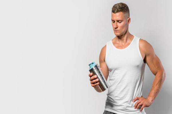 Batidos de proteína y calvicie - hombre musculado con un bote para batido de proteínas en la mano
