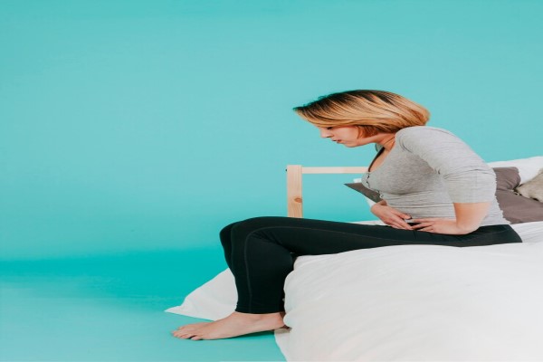 hirsutismo hormonal - mujer sentada en la cama palpando su abdomen