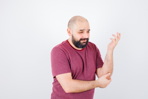hombre con problemas graves de alopecia con cara de dolor mientras se sujeta el codo con la mano