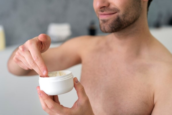 hombre sonriente preparándose para aplicar cera en su cabello en vez de gomina