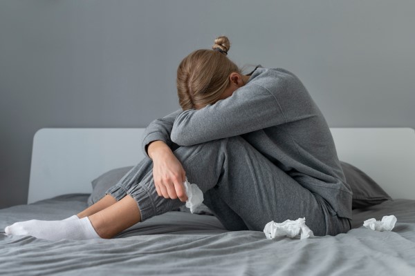 mujer deprimida sentada en la cama con varios pañuelos en la cama y su cara entre los brazos