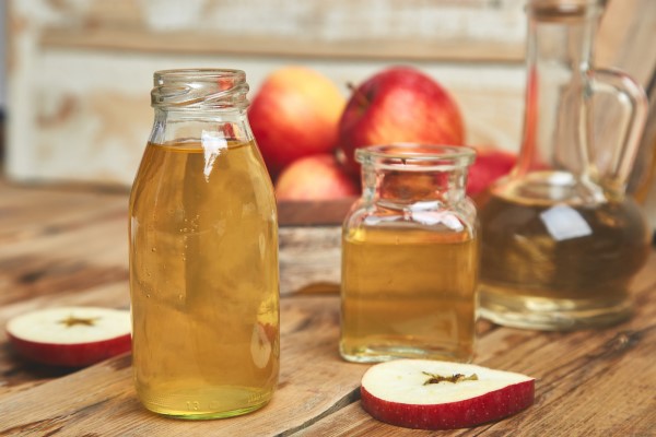  botes de cristal con vinagre de manzana sobre una mesa con rodajas de manzana