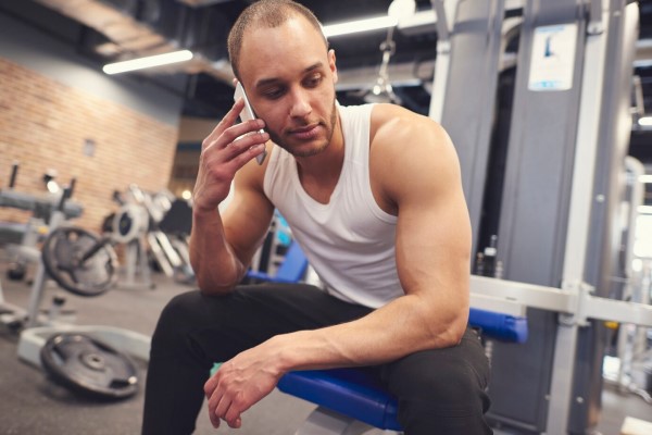 hombre hablando por teléfono en el gimnasio con signos de alopecia en las entradas y la línea del cabello