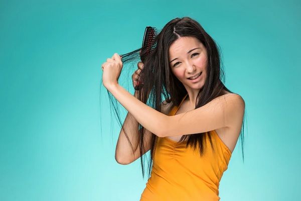 Trichorrhexis Nudosa - joven con cara de sufrimiento mientras desenreda su cabello con un cepillo
