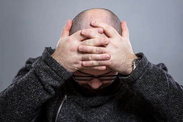 diagnosticar la alopecia - hombre mirando hacia el suelo mientras se lleva las manos a la cabeza con claros signos de alopecia