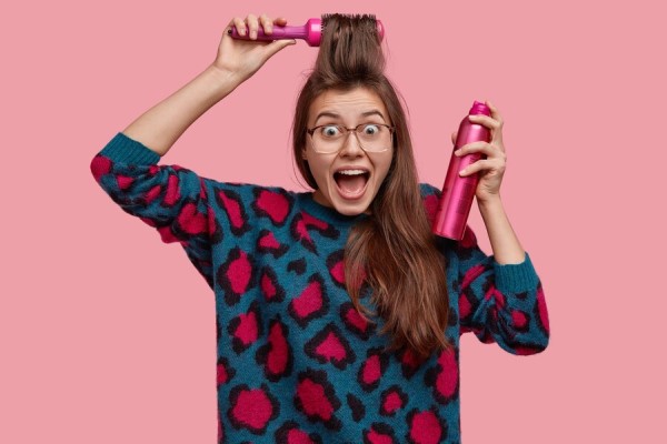 fijadores de pelo - mujer alegre peinando su cabello con un cepillo en una mano y un spray con un fijador capilar en la mano