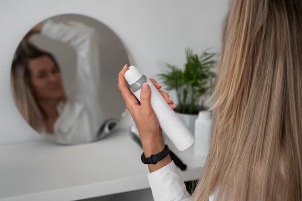 mujer delante del espejo peinando su melena con la ayuda de un fijador para el cabello