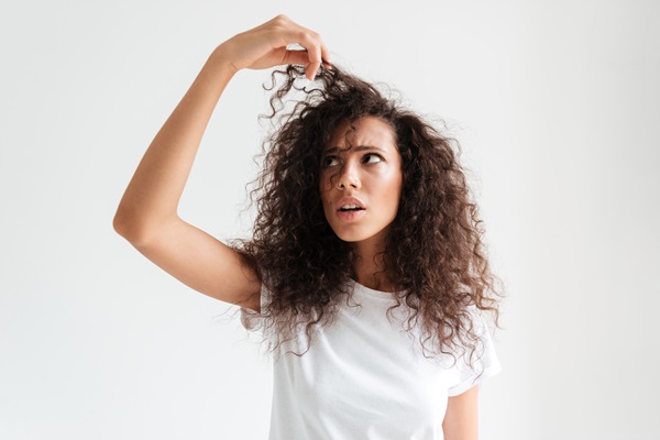 Mujer joven asombrada sosteniendo con la mano su cabello reseco y con frizz