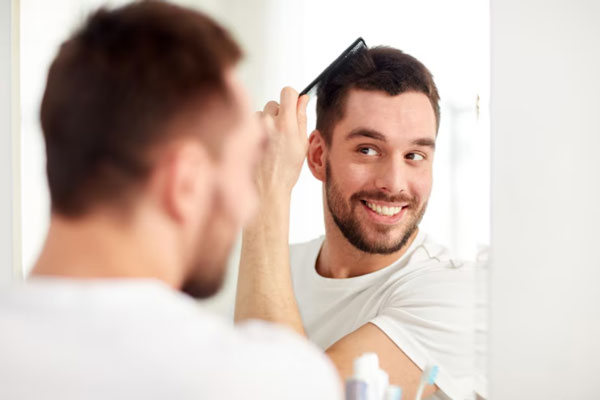 Hombre sonriente peina su cabello frente al espejo tras recuperar su densidad capilar 
