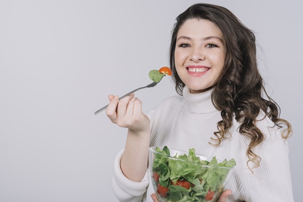 Vegetariano - Mujer joven sosteniendo un cubierto y recipiente de cristal con frutas y hortalizas