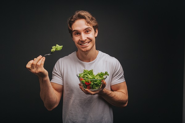 Hombre joven sosteniendo un tenedor y envase de vidrio con lechugas y frutas