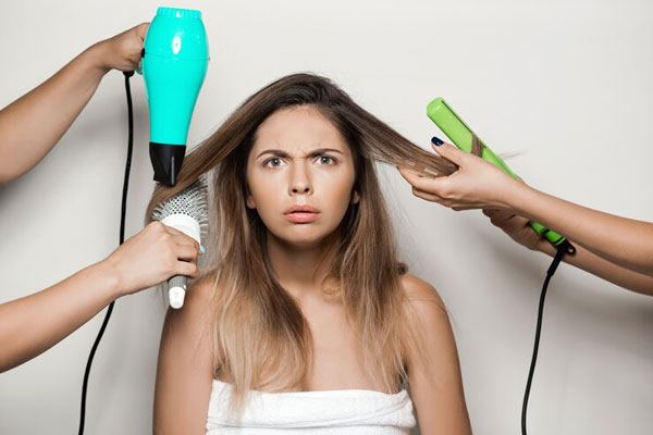 Peinados que debes evitar - Joven con cabello reseco se percata de los daños ocasionados por el uso excesivo de la plancha y el secador
