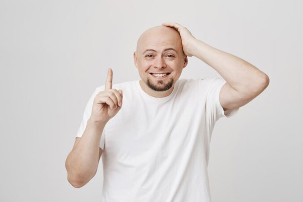 287 genes - Hombre con alopecia androgénica sonríe mientras lleva su mano a la cabeza 
