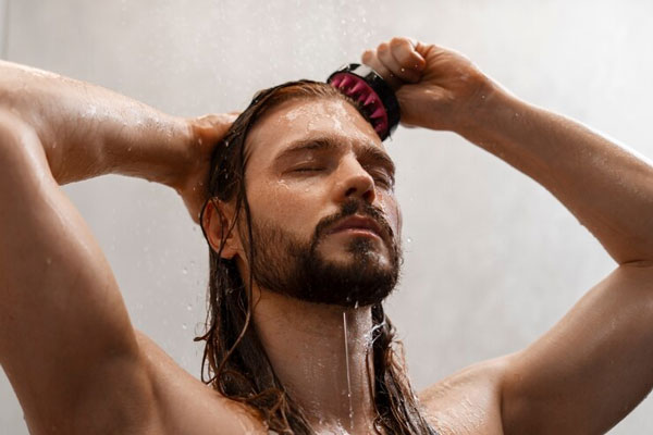 Hombre de cabello largo aplica masajes sobre el cuero cabelludo mientras se ducha 