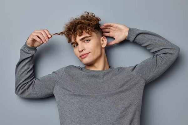 el pelo - joven tumbado estirando uno de los rizos de su melena encrespada por culpa del pelo quemado