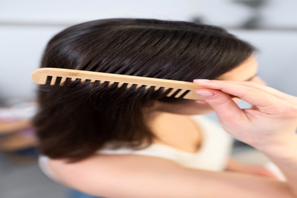 joven peinándose el cabello con un peine de madera con dientes anchos para mejorar el desenredo del cabello