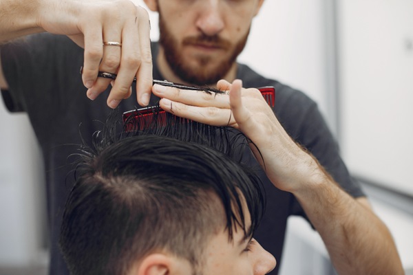 Cortes de pelo para hombres - Estilista cortando el cabello de un hombre utilizando tijeras para hacer un corte de flequillo