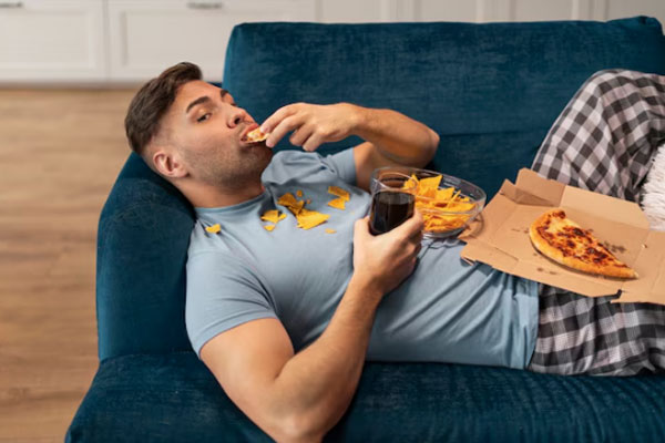 Hombre con malos hábitos alimenticios y problemas capilares come comida chatarra sobre el sofá 