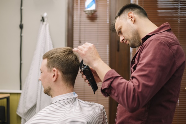 Estilista usando una máquina de afeitar para cortar el cabello de un cliente masculino