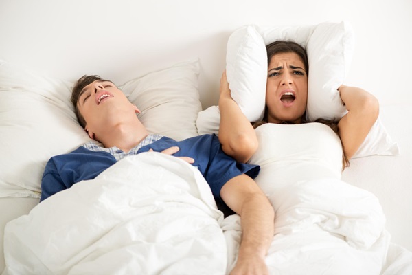 Roncar provoca alopecia - Mujer con cara de molestia tapándose los oídos con la almohada debido a los ronquidos de la pareja
