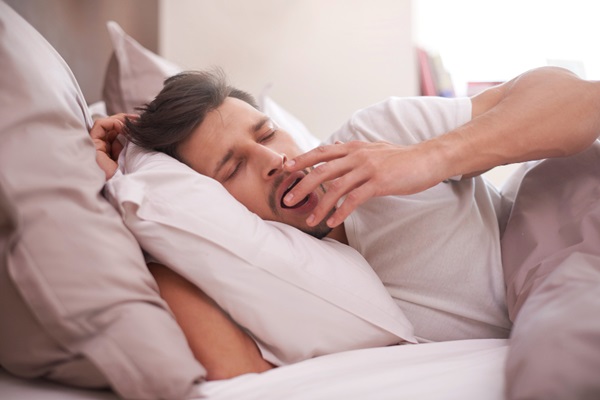 Hombre acostado en la cama con varias almohadas bostezando antes de dormir