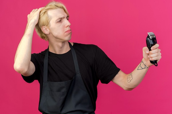 Teñirse el pelo tras injerto capilar - Hombre indecisión tocándose el cabello de color rubio mientras sostiene en la mano una máquina de afeitar