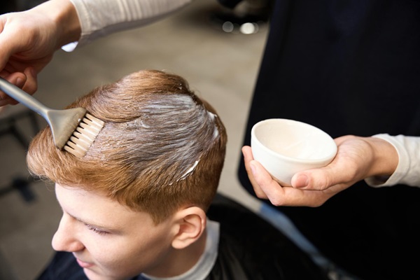 Teñirse el pelo tras injerto capilar - Estilista utilizando una brocha para teñir el pelo de un hombre joven
