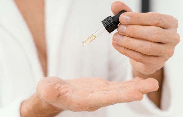 manos de hombre con un cuentagotas con aceites esenciales para el cuidado del pelo injertado