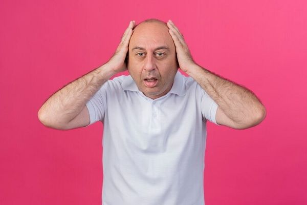 Consecuencias psicológicas de la alopecia- Hombre sobre fondo rosa, preocupado por su alopecia