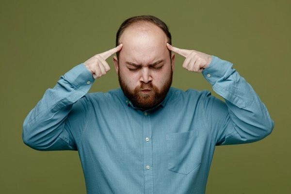 Consecuencias psicológicas de la alopecia- Hombre con problemas de calvicie en la parte frontal y coronilla, toca su cabeza con preocupación