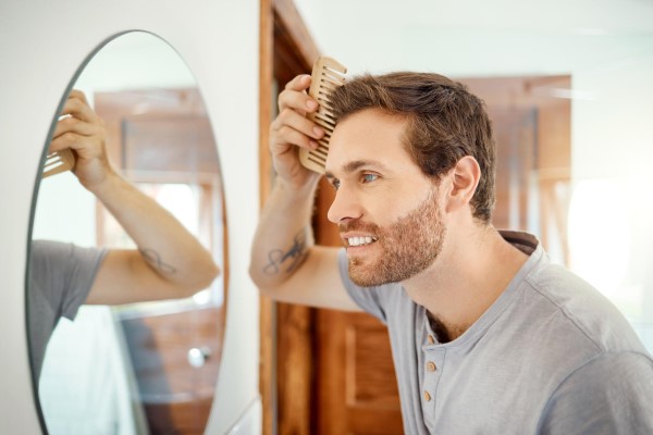 peinar el pelo después del trasplante capilar - hombre delante del espejo se cepilla el cabello para el mantenimiento del crecimiento