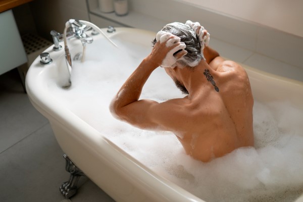 hombre en la bañera enjabonando la cabeza con sumo cuidado
