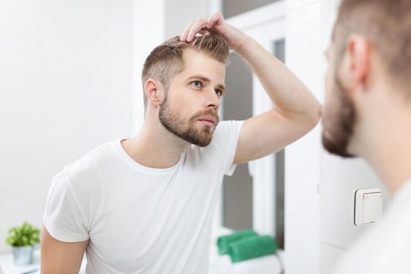 hombre rubio revisa su pelo en un espejo