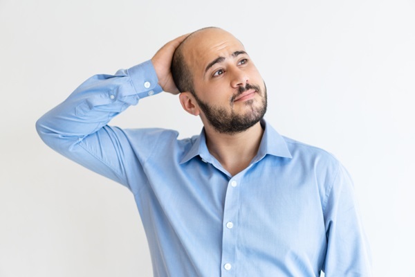 Trasplante de pelo corporal - Hombre con alopecia avanzada y barba abundante tocando su cabeza con la mano