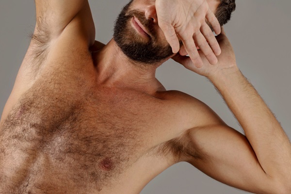 Trasplante de pelo corporal - Hombre con abundante pelo en el pecho y barba tapándose la cara con las manos