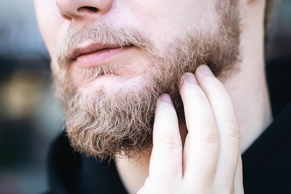 Trasplante de pelo corporal - Hombre tocando con la mano su barba de color castaño luego de un injerto de vello corporal