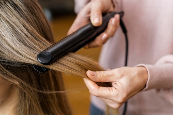Alisar el cabello - Estilista utilizando una plancha para alisar el pelo de una mujer en la peluquería