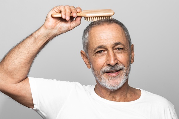 Injerto de pelo con canas - Hombre sosteniendo en su cabeza un cepillo para peinar su cabello con canas