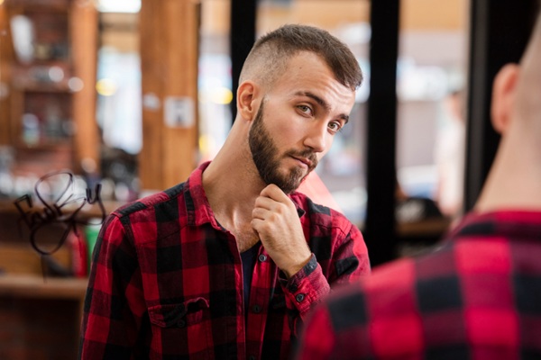 Cortes de pelo para calvos - Hombre mirándose al espejo luego de realizarse un corte de cabello para calvos que ayuda a cubrir las zonas con alopecia