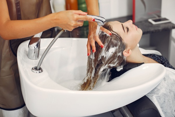 Cuidados para embellecer el cabello - Estilista lavando el cabello de una mujer con abundante champú para limpiar el cuero cabelludo