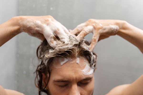 Cuidados para embellecer el cabello - Hombre lavando su cabello con abundante champú para eliminar el exceso de sebo siguiendo los cuidados capilares adecuados