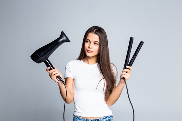 Cuidados para embellecer el cabello - Mujer joven sosteniendo en sus manos un secador de pelo y una plancha para cabello que pueden causar daños capilares